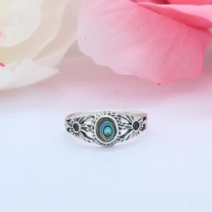 May include: A silver ring with a blue and green abalone shell inlay. The ring has a floral design with three flower accents.