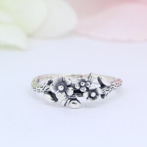 May include: A silver ring with a floral design. The ring features three flowers with delicate details and a textured stem.