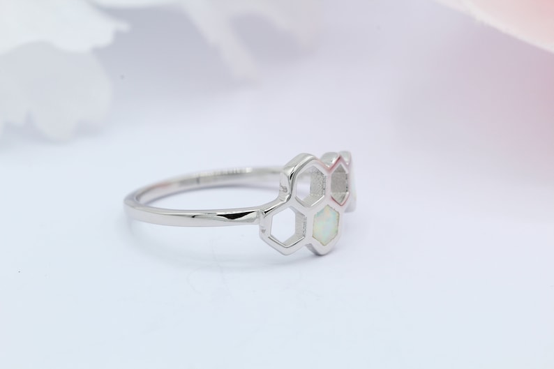 May include: A silver ring with a honeycomb design featuring white opal stones.