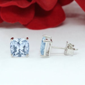 May include: A pair of silver stud earrings with light blue square-shaped gemstones.