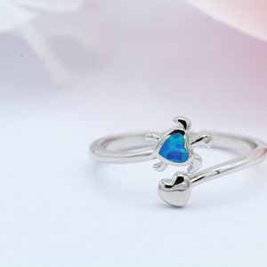 May include: A silver ring with a blue opal heart and a turtle design.