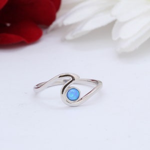 May include: A silver ring featuring a blue opal gemstone set in a wave design.