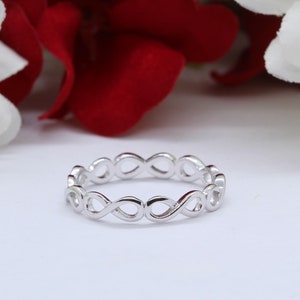 May include: A silver infinity symbol ring with a delicate design. The ring is made of smooth, polished metal and has a simple, elegant look.