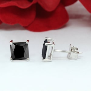 May include: A pair of silver stud earrings with black square-shaped gemstones.