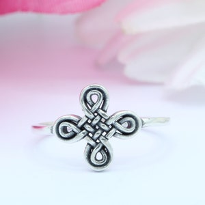 May include: A silver ring with a Celtic knot design. The knot is in the shape of a cross.