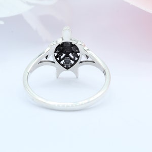 May include: A silver ring with a detailed turtle design. The turtle is centered on the ring and has a black finish. The ring is on a white background.