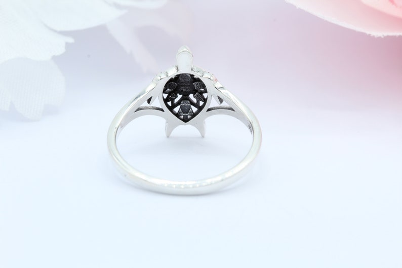 May include: A silver ring with a detailed turtle design. The turtle is centered on the ring and has a black finish. The ring is on a white background.