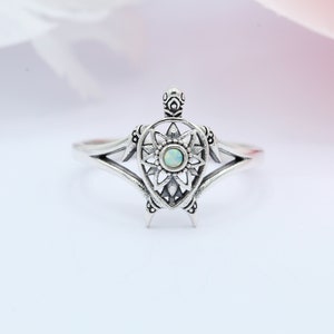 May include: A silver ring with a detailed turtle design featuring an opal gemstone in the center.
