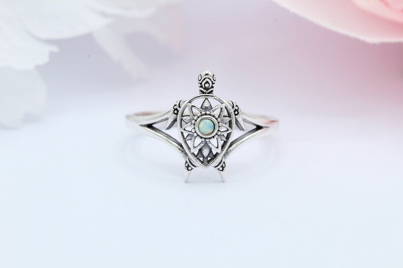 May include: A silver ring with a detailed turtle design featuring an opal gemstone in the center.