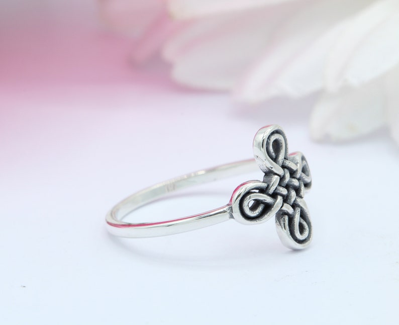 May include: A silver ring with a Celtic knot design. The knot is a four-leaf clover shape.