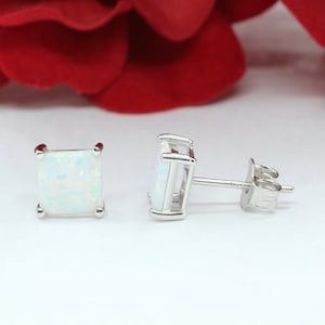 May include: A pair of silver earrings with square white opal gemstones. The earrings have a post and butterfly back.
