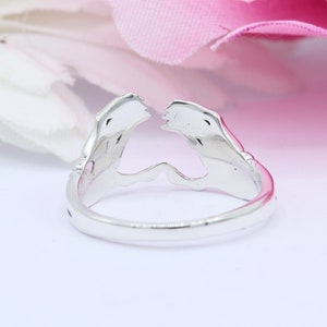 May include: Silver ring with a design of two hands clasped together, forming a heart shape.