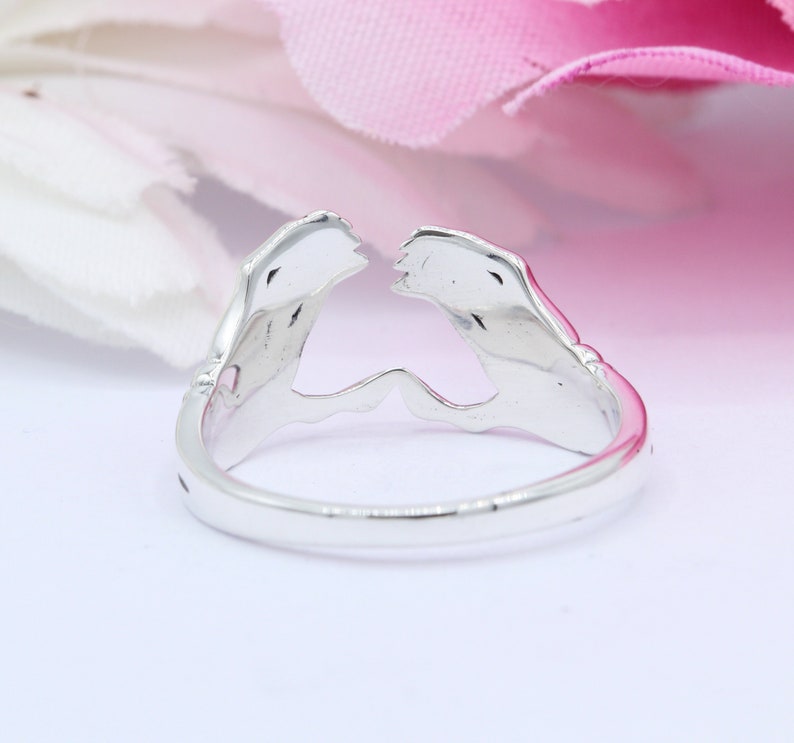 May include: Silver ring with a design of two hands clasped together, forming a heart shape.