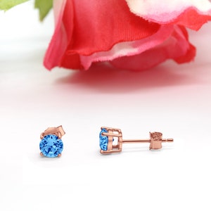 May include: A pair of rose gold stud earrings with a blue gemstone in each earring.
