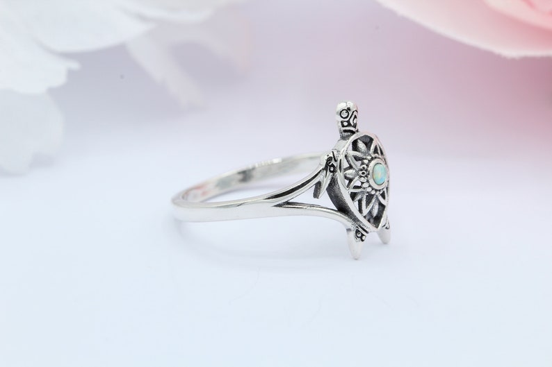 May include: A silver ring featuring a detailed turtle design with an opal gemstone in the center. The ring has a delicate, openwork design and a smooth band.