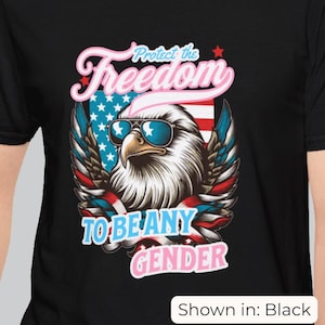 Op de afbeelding: Zwart T-shirt met een afbeelding van een adelaar met zonnebril, tegen een ontwerp van de Amerikaanse vlag. De tekst luidt: "Protect the Freedom to be any Gender."