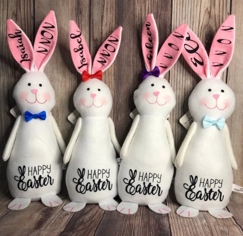 May include: Four white plush Easter bunny decorations with pink ears. Each bunny has a different name on its ears: Isaiah, Isabel, Eileen, and El. Each bunny has a blue bow tie and the text "Happy Easter" on its belly.