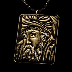 May include: A gold-toned pendant necklace featuring a detailed relief sculpture of a man's face. The man is wearing a turban and has a beard. The pendant is rectangular in shape.