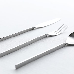 Puede incluir: Un juego de tres cubiertos de plata, que incluye un cuchillo, un tenedor y una cuchara, con un diseño minimalista.