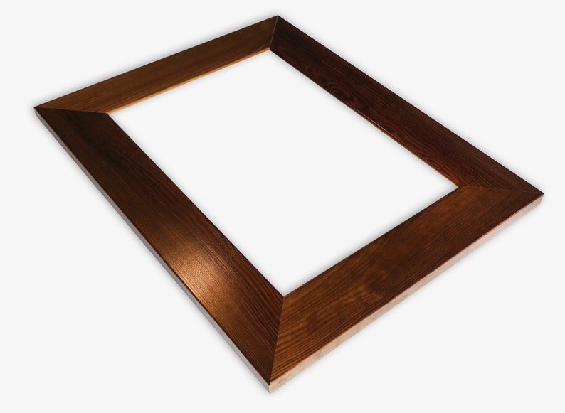 Puede incluir: Un marco de fotos rectangular de madera marr&oacute;n oscuro. El marco presenta una veta de madera visible y bordes biselados. El &aacute;ngulo muestra el espacio interior. La madera tiene un tono c&aacute;lido.