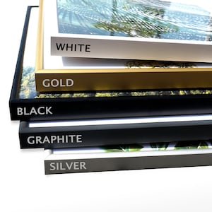 May include: Five picture frames stacked on top of each other. The frames are in different colors: white, gold, black, graphite, and silver. The frames are all the same size and shape.