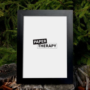 May include: Black picture frame with a white mat and the text "PAPER THERAPY" in black letters.