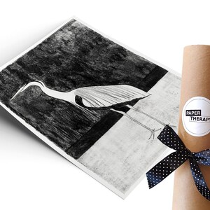 May include: A black and white illustration of a heron printed on white paper, rolled up and tied with a black ribbon with white polka dots. The paper is labelled "Paper Therapy".