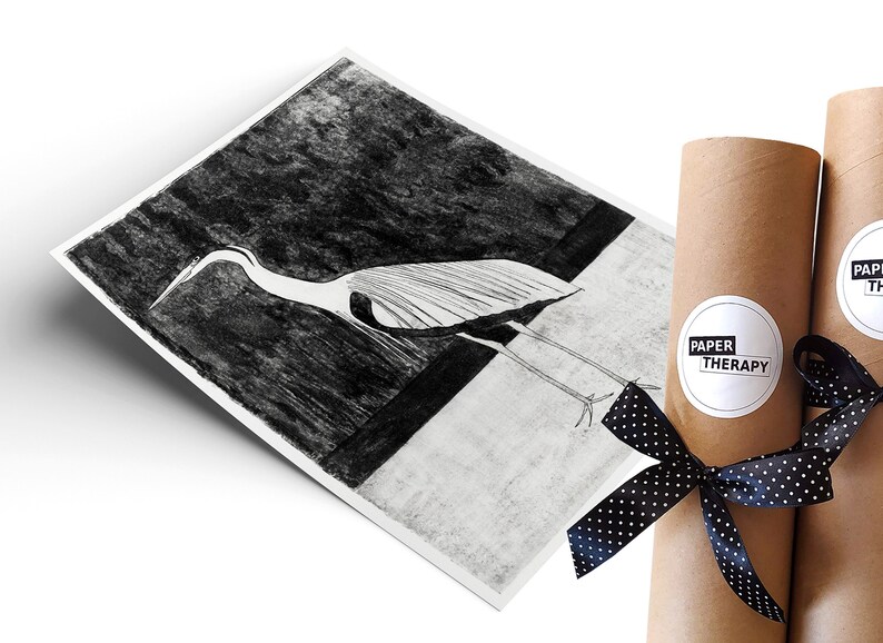 May include: A black and white illustration of a heron printed on white paper, rolled up and tied with a black ribbon with white polka dots. The paper is labelled "Paper Therapy".