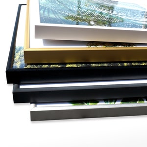 May include: A stack of five picture frames in different colors and sizes. The frames are made of wood and have a simple design. The top frame is white, the second is gold, the third is black, the fourth is dark gray, and the bottom frame is silver.
