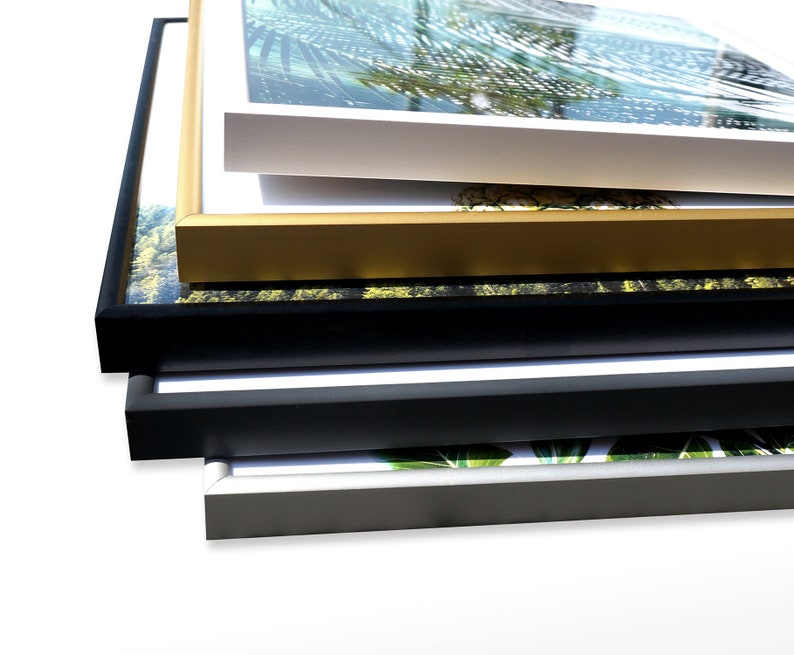 May include: A stack of five picture frames in different colors and sizes. The frames are made of wood and have a simple design. The top frame is white, the second is gold, the third is black, the fourth is dark gray, and the bottom frame is silver.