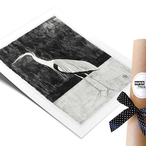 May include: Black and white illustration of a heron standing on a white surface with a dark background. The illustration is printed on a white paper and rolled up in a brown tube with a black and white polka dot ribbon and a white sticker with the text "PAPER THERAPY".