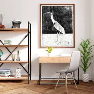 May include: A black and white illustration of a heron in a wooden frame hangs above a wooden desk with a white chair. A potted plant sits on the floor next to the desk.