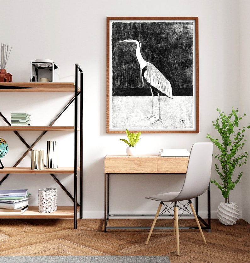 May include: A black and white illustration of a heron in a wooden frame hangs above a wooden desk with a white chair. A potted plant sits on the floor next to the desk.