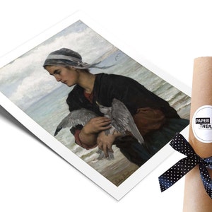 May include: A painting of a woman in a blue and white headscarf holding a seagull in her arms. The woman is standing on a beach with the ocean in the background. The painting is in a white frame.