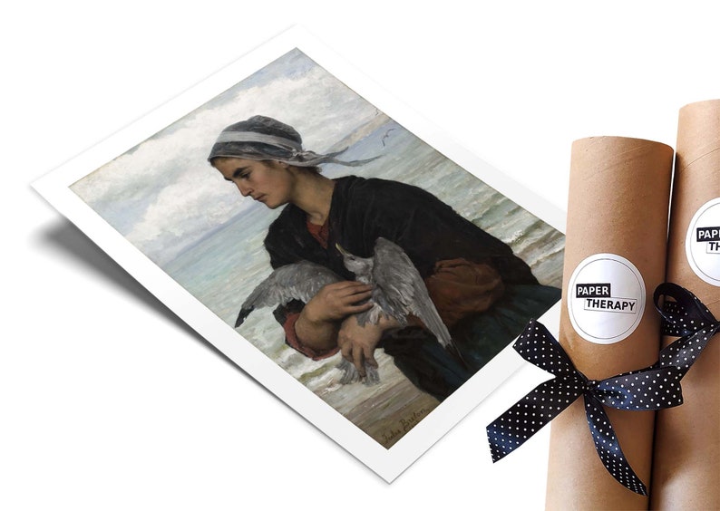 May include: A painting of a woman in a blue and white headscarf holding a seagull in her arms. The woman is standing on a beach with the ocean in the background. The painting is in a white frame.
