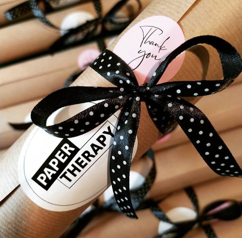 May include: A brown paper tube with a black and white polka dot ribbon tied around it. The tube has a white sticker with the text "PAPER THERAPY" on it. A pink sticker with the text "Thank you" is also on the tube.
