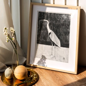 May include: A framed black and white print of a heron standing on a black background. The frame is made of light wood and has a white mount.