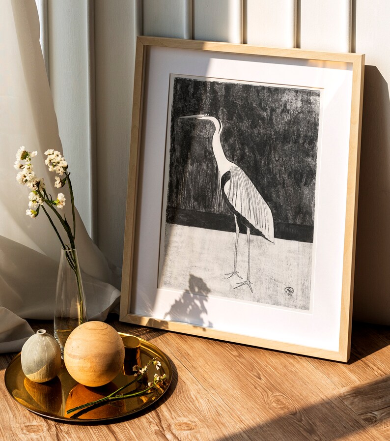 May include: A framed black and white print of a heron standing on a black background. The frame is made of light wood and has a white mount.