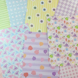 May include: A collection of patterned papers in various colors. Designs include witch hats, pumpkins, eyeballs, and stripes. Colors include light blue, pink, purple, yellow, and green. The papers are arranged in a layered, overlapping fashion.