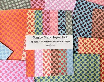 Op de afbeelding: Een verzameling van A5-formaat papier met diverse sterpatronen in verschillende kleuren, waaronder roze, blauw, oranje, groen en bruin. Een wit label op de voorzijde bevat de tekst Simple Stars Paper Pack, A5 size - 12 Assorted Patterns - 120gsm, MAIL MAGIC.