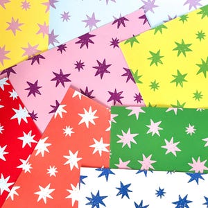 Peut inclure: Une collection de feuilles de papier colorées avec des motifs d'étoiles. Les feuilles sont de différentes couleurs, dont le jaune, le rose, le rouge et le vert. Les étoiles sont de couleurs contrastées, comme le violet, le blanc et le bleu. Vue de dessus.