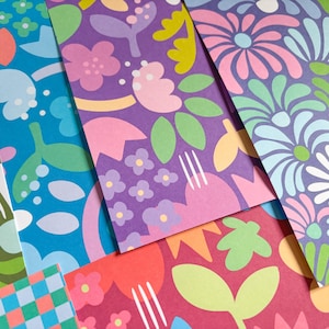 May include: A selection of patterned papers with floral designs. The papers display flowers, leaves, and abstract shapes in shades of blue, purple, pink, green, and red. Some papers have a checkered pattern.