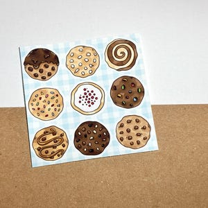 Op de afbeelding: Een vierkante sticker met negen geïllustreerde koekjes met verschillende toppings en ontwerpen. De koekjes zijn gerangschikt op een lichtblauwe en witte geruite achtergrond. De koekjes bevatten chocoladechips, hagelslag en wervelontwerpen.