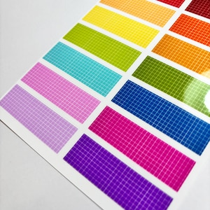 May include: A sheet of colourful grid sticker strips. Each strip is a different colour, including red, orange, yellow, green, blue, pink, and purple. The grid pattern is white, and the stickers are on a white background.