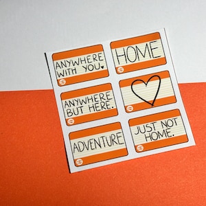 Pode incluir: Uma folha de autocolantes laranja e brancos com texto preto. Os autocolantes apresentam frases como "Anywhere with you", "Home" e "Adventure". Um coração preto é desenhado num autocolante. O fundo é branco e laranja.