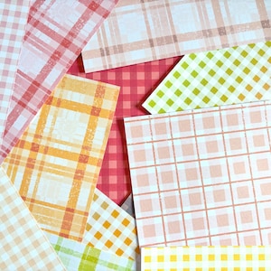 Puede incluir: Una colección de hojas de papel rectangulares superpuestas con varios patrones, incluyendo cuadros vichy en rosa, naranja y verde lima, así como diseños de tartán multicolor en tonos pastel suaves y una hoja de cuadros vichy roja.