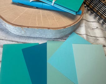 May include: Assortment of five cardstock paper sheets in various shades of blue and green. The paper is smooth and has a matte finish.