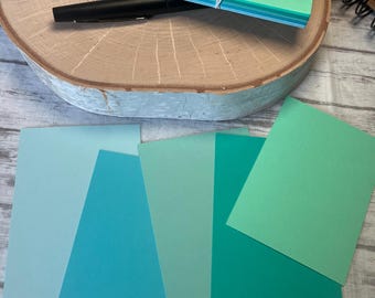 May include: Five different shades of blue and green cardstock paper. The paper is arranged in a fan shape. The paper is smooth and has a matte finish.