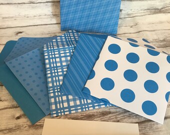 May include: A set of six blue and white patterned envelopes with a blue pen and a blank white card. The envelopes have different patterns including polka dots, stripes, and plaid.
