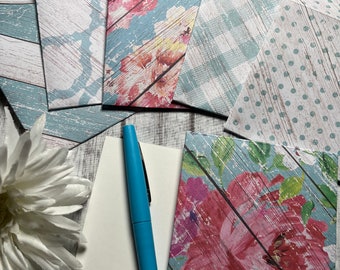May include: A set of six decorative envelopes with a blue and white woodgrain pattern and floral designs. The envelopes are arranged on a white wooden surface with a blue pen and a white flower.